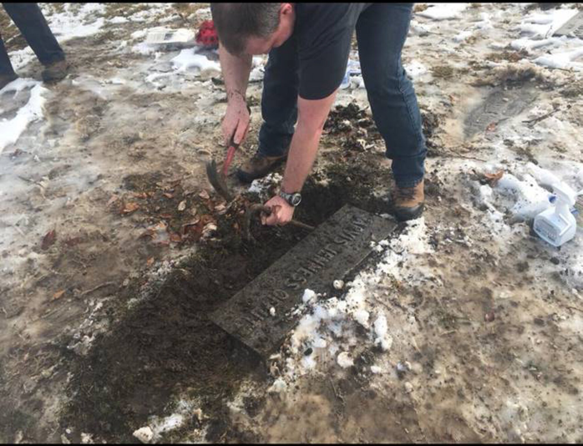 Royal Air Force Master Aircrew Keith Wing, 56 Squadron Rivet Joint specialist, uses a hammer and crowbar to reveal the inscription on U.S. Army 1st Lt. Jarvis Offutt's grave February 2018, at Forrest Lawn Memorial Park, Nebraska.