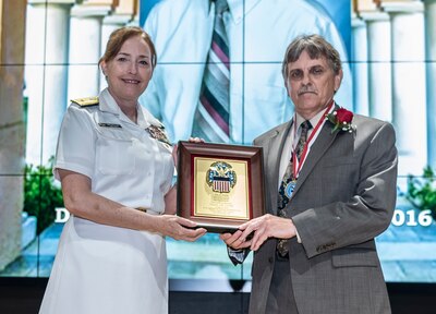 Harvey P. Hodak receives a plaque and medal from Defense Logistics Agency Land and Maritime Commander Navy Rear Adm. Michelle Skubic.