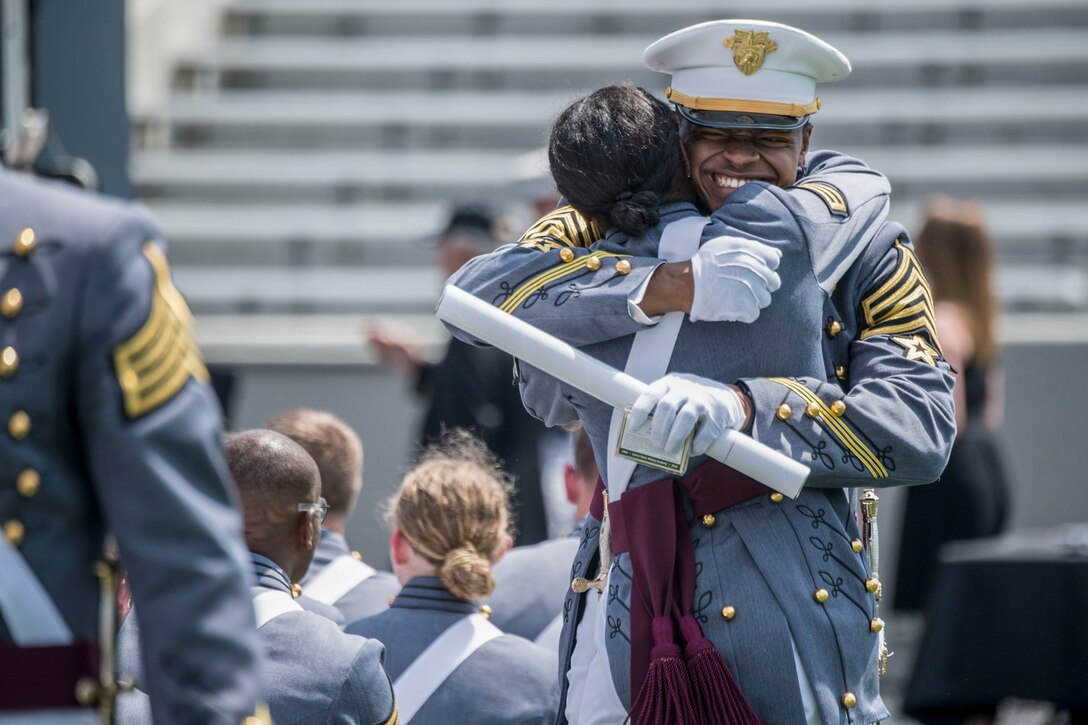 A U.S. Military Academy clutching a diploma smiles and hugs another cadet.