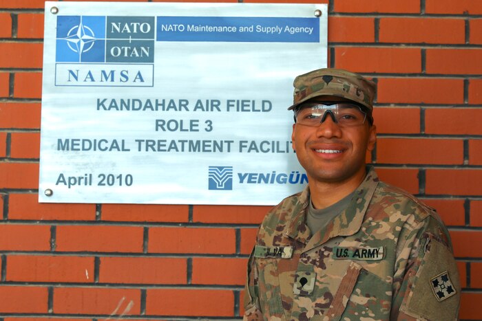 A soldier poses for a photo in front of a rad brick wall.