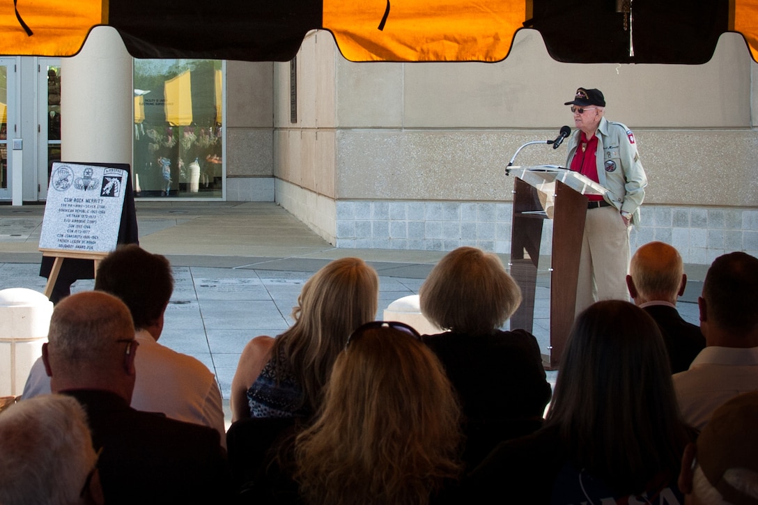 A veteran speaks at a lectern to an audience outside.