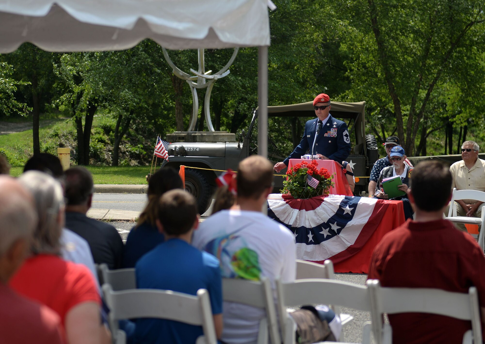 A man in the Air Force service dress uniform and a red beret speaks to a crowd.