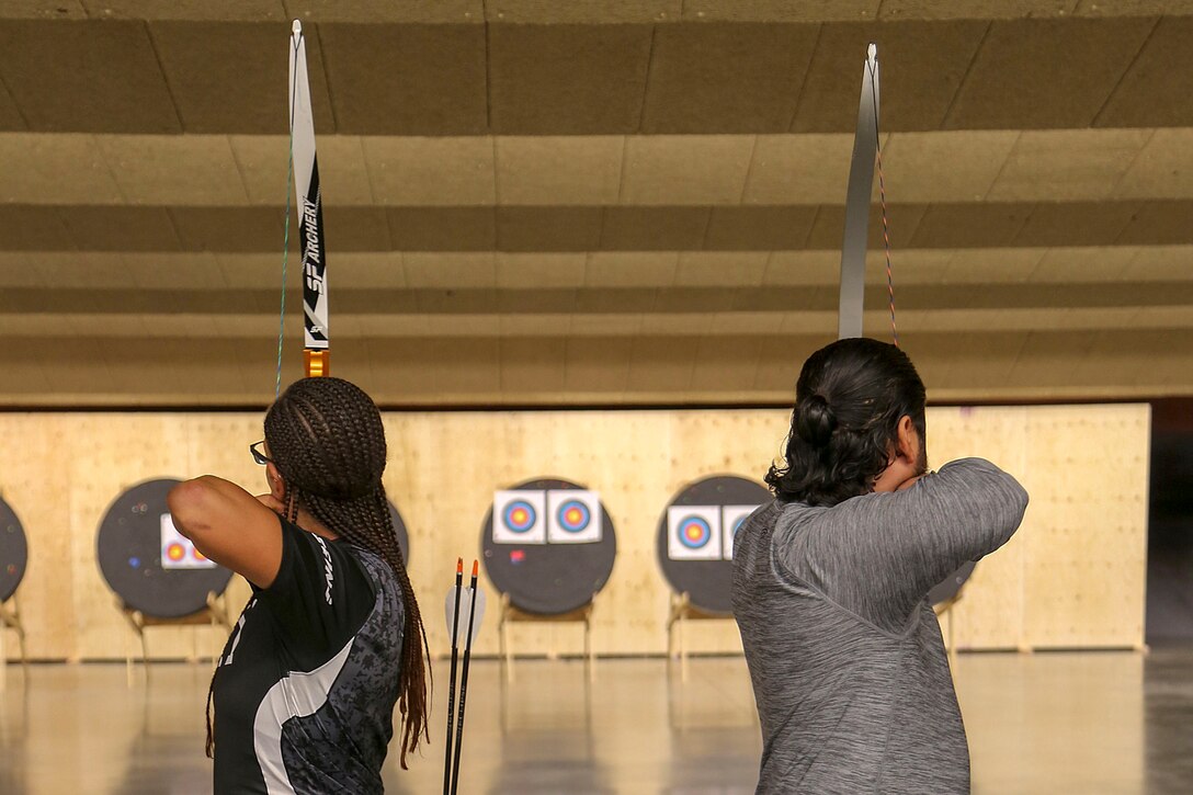 Two archers, shown from behind, pull back arrows while aiming at targets.