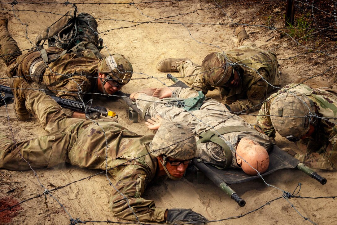 Soldiers transport a mock casualty under a barbed wire obstacle.