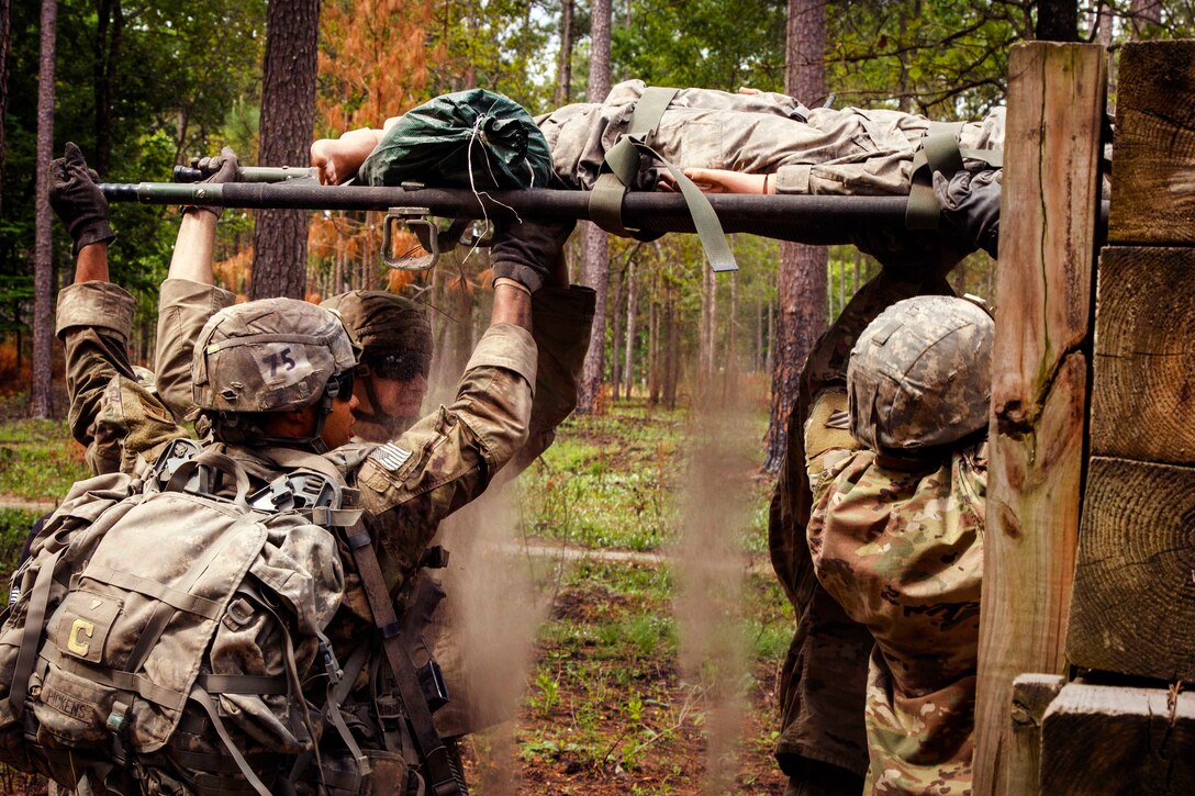 Soldiers pass a mock casualty over a barrier obstacle.