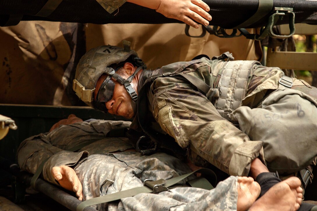 A soldier positions and secures a mock casualty in the back of a military vehicle.