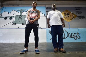 Senior Airman Jordan Guthrie, left, 437th Aerial Port Squadron passenger travel technician, and William Brown III, right, 437th APS packing crate supervisor, stand in front of a 437th APS mural here May 17, 2018. Guthrie designed the art for the mural and painted the entire piece with the help of Brown. The mural highlights the “Port Dawgs” heritage. Guthrie has been drawing and practicing art since he was 10 years old.