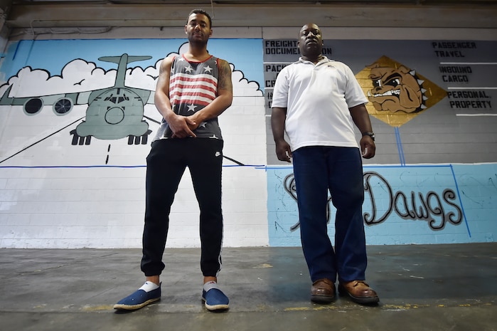 Senior Airman Jordan Guthrie, left, 437th Aerial Port Squadron passenger travel technician, and William Brown III, right, 437th APS packing crate supervisor, stand in front of a 437th APS mural here May 17, 2018. Guthrie designed the art for the mural and painted the entire piece with the help of Brown. The mural highlights the “Port Dawgs” heritage. Guthrie has been drawing and practicing art since he was 10 years old.