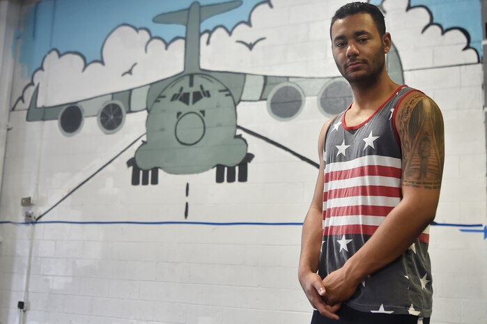 Senior Airman Jordan Guthrie, 437th Aerial Port Squadron passenger travel technician, stands in front of a 437th APS mural here May 17, 2018. Guthrie designed the art for the mural and painted the entire piece with the help of William Brown III, 437th APS packing crate supervisor. The mural highlights the “Port Dawgs” heritage. Guthrie has been drawing and practicing art since he was 10 years old.