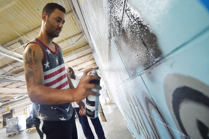 Senior Airman Jordan Guthrie, foreground, 437th Aerial Port Squadron passenger travel technician, and William Brown III, background, 437th APS packing crate supervisor, paint part of a 437th APS mural here May 17, 2018. Guthrie designed the art for the mural and painted the entire piece with the help of Brown. The mural highlights the “Port Dawgs” heritage. Guthrie has been drawing and practicing art since he was 10 years old.
