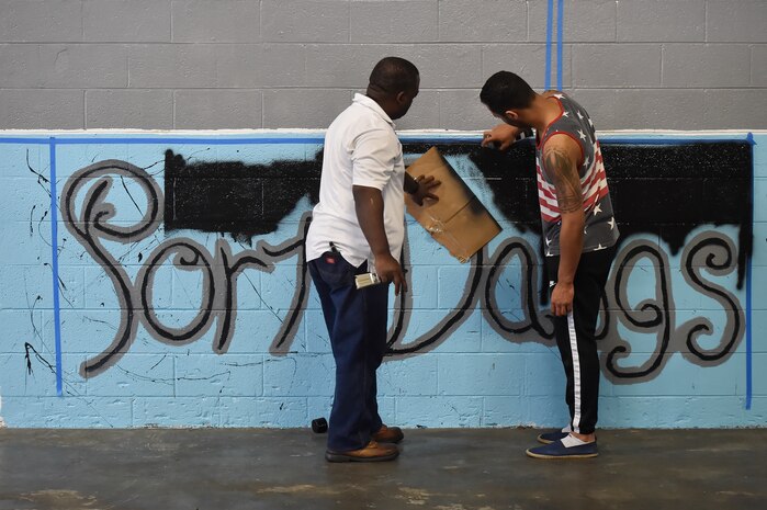 Senior Airman Jordan Guthrie, right, 437th Aerial Port Squadron passenger travel technician, and William Brown III, left, 437th APS packing crate supervisor, paint part of a 437th APS mural here May 17, 2018. Guthrie designed the art for the mural and painted the entire piece with the help of Brown. The mural highlights the “Port Dawgs” heritage. Guthrie has been drawing and practicing art since he was 10 years old.