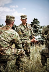 Caucasian male Chaplain CPT Stene kneeling whle delivering a sermon to group of Soldiers wearing OCP outside during the day.