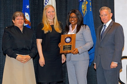 Navy Cyber Security Division Director Rear Adm. Danelle Barrett (OPNAV N2N6G), left, Acting Department of the Navy (DON) Chief Information Officer (CIO) Dr. Kelly Fletcher, second from left, and Marine Corps Acting Director C4 and CIO Ken Bible, right, present a DON Information Management/Information Technology (IM/IT) Excellence Award to Space and Naval Warfare Systems Center (SSC) Atlantic computer scientist Brianeisha Eure at the DON IT East Conference April 24, 2018, in Norfolk, Va.