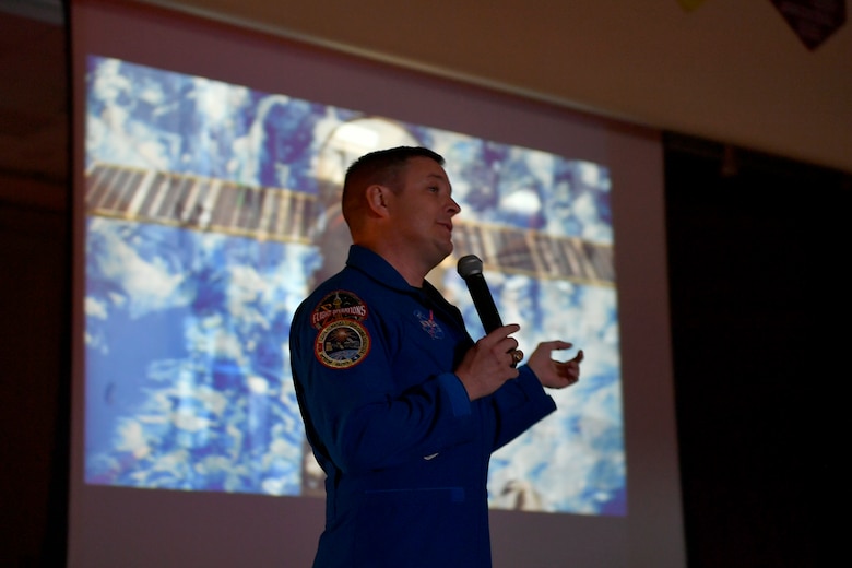 Col. Jack “2 Fish” Fischer, NASA astronaut, gives a presentation in front of a projector screen playing footage from his missions, May 22, 2018, at Aurora Quest K-8 School, Aurora, Colorado. Fischer’s speech was a surprise for nearly 600 students at Aurora Quest K-8 School, who thought they would be attending a general assembly. (U.S. Air Force photo by Senior Airman Madison J. Ratley)