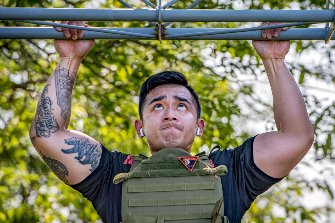 A sailor looks up while doing a pullup with trees in the background.