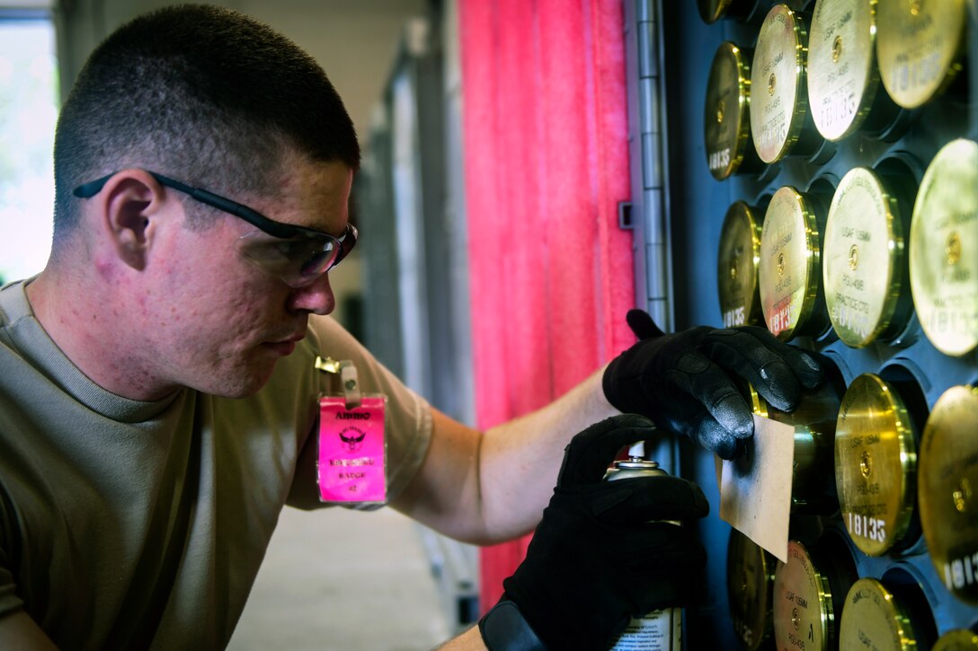 A technician spray paints a 105-mm target practice round.