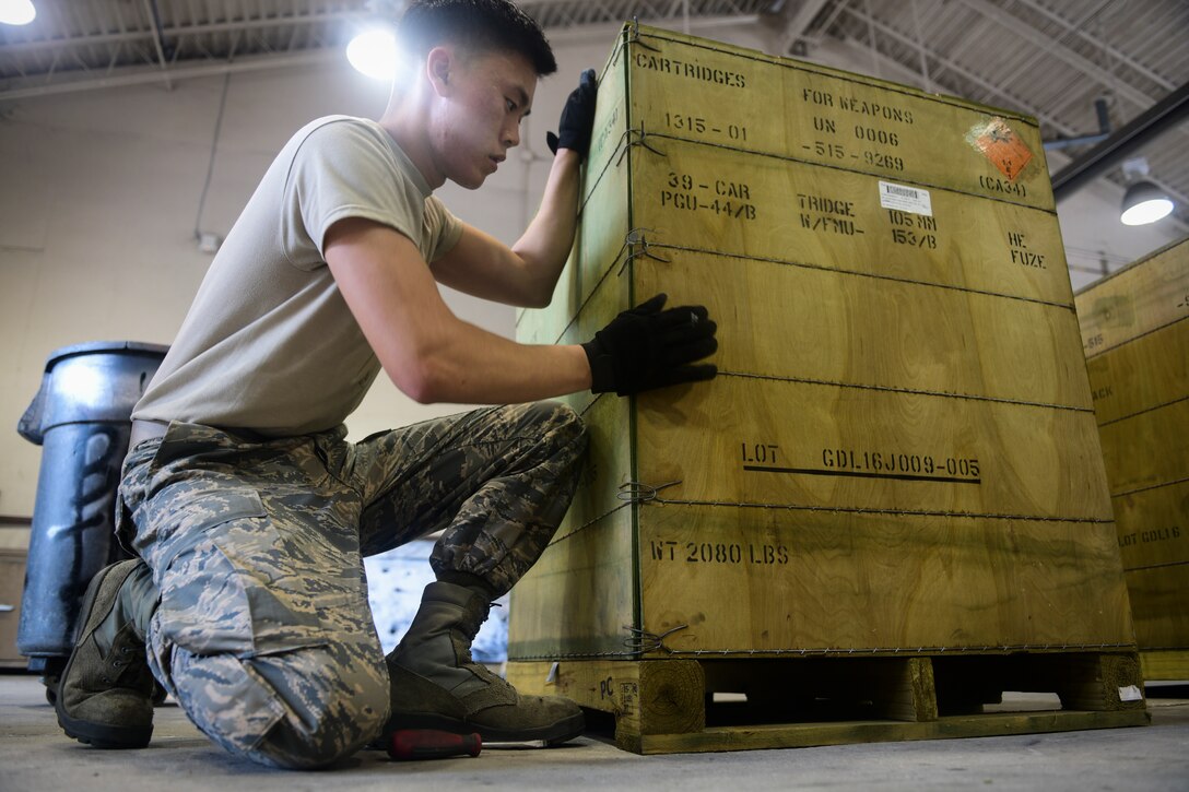 An airman opens a crate of 105-mm high explosive rounds.