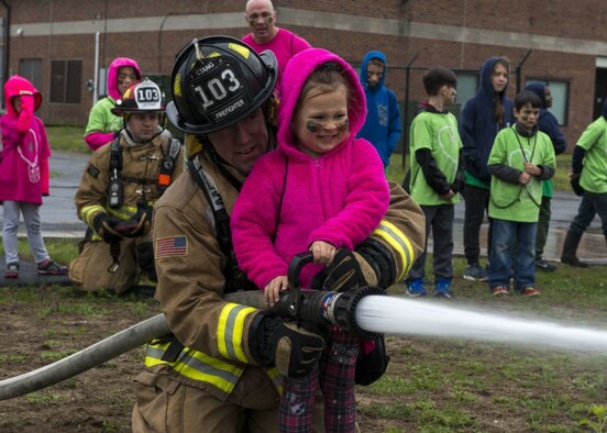 A firefighter assigned to the 103rd Airlift Wing helps a young girl spray a fire hose May 19, 2018.