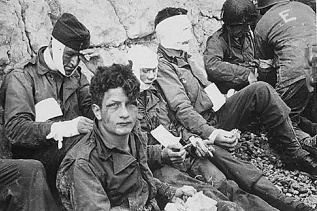 Wounded soldiers sit on a beach.