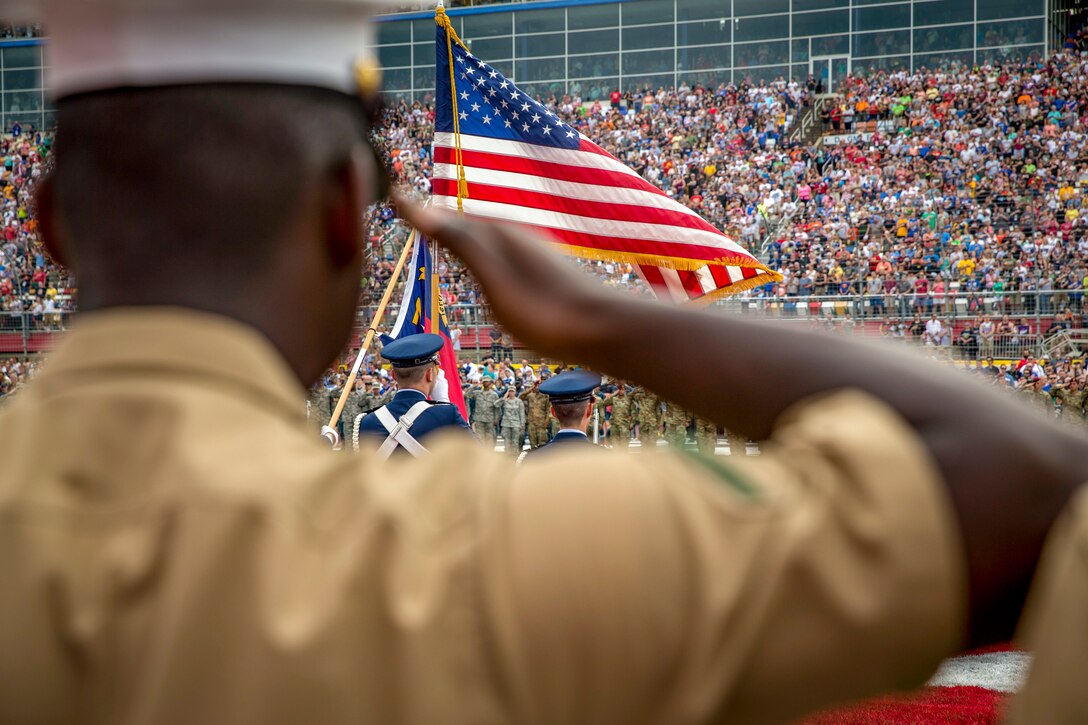 A Marine salutes toward an American flag at a stadium.