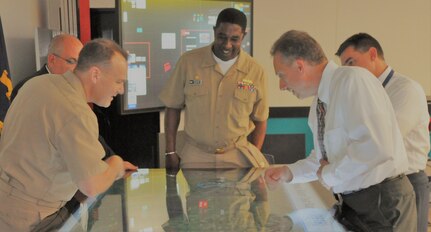 IMAGE: DAHLGREN, Va. (May 31, 2018) - Naval Surface Warfare Center Dahlgren Division (NSWCDD) Innovation Lab (iLab) Director of Innovation Nelson Mills briefs NSWC Commander Rear Adm. Thomas Anderson, left, on the use of digital collaboration tables as visual aids for surface ships. The collaboration table could provide capabilities to view ship doctrine, navigation tracks, radar information, and Automatic Identification System information for situational awareness. The iLab - equipped with state-of-the-art equipment, services, and trained personnel - is an intensive collaborative environment where the command's experts work to speed up and maximize corporate innovative solutions across the laboratory. NSWCDD Commanding Officer Capt. Godfrey 'Gus' Weekes looks on from the center. Standing behind the admiral is NSWCDD Technical Director John Fiore and standing behind Mills is NSWCDD Deputy Technical Director Dale Sisson.