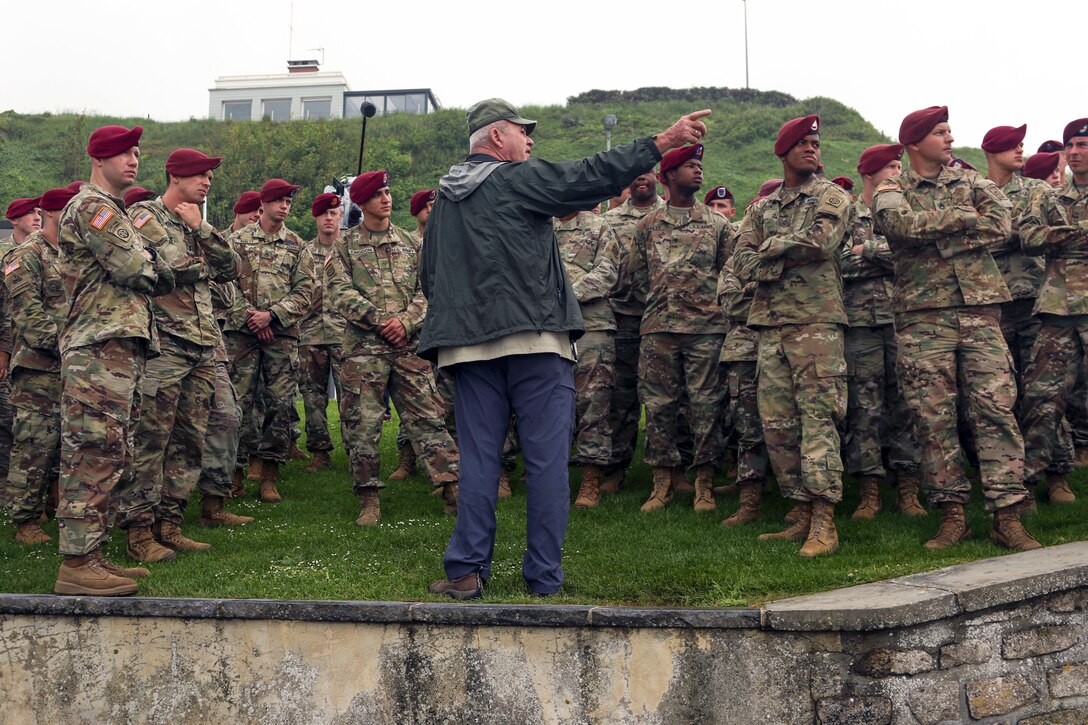 A man standing in front of a group of soldiers on a grassy area points something out to them.