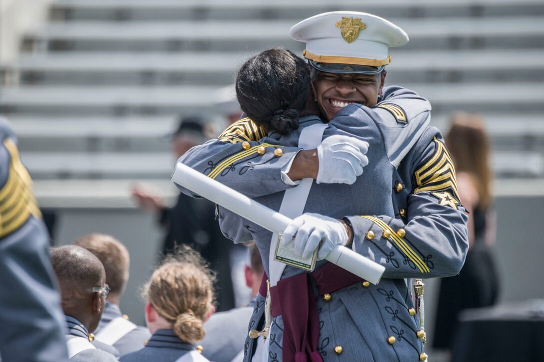 A U.S. Military Academy cadet clutching a diploma smiles and hugs another cadet.