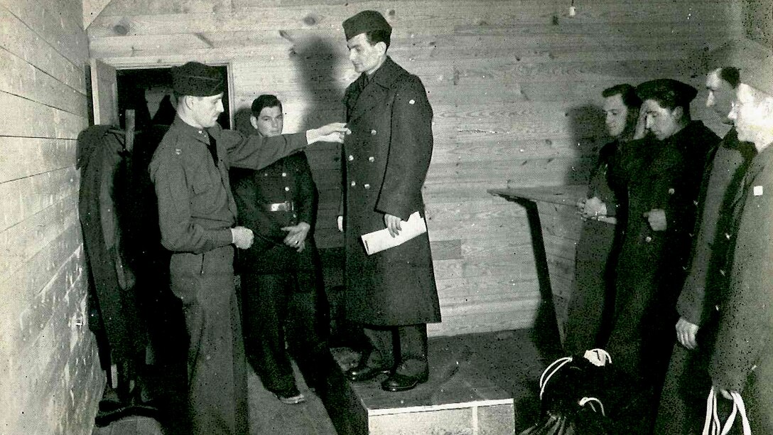 A historic photo of a soldier standing on a small platform being inspected after receiving his official uniform
