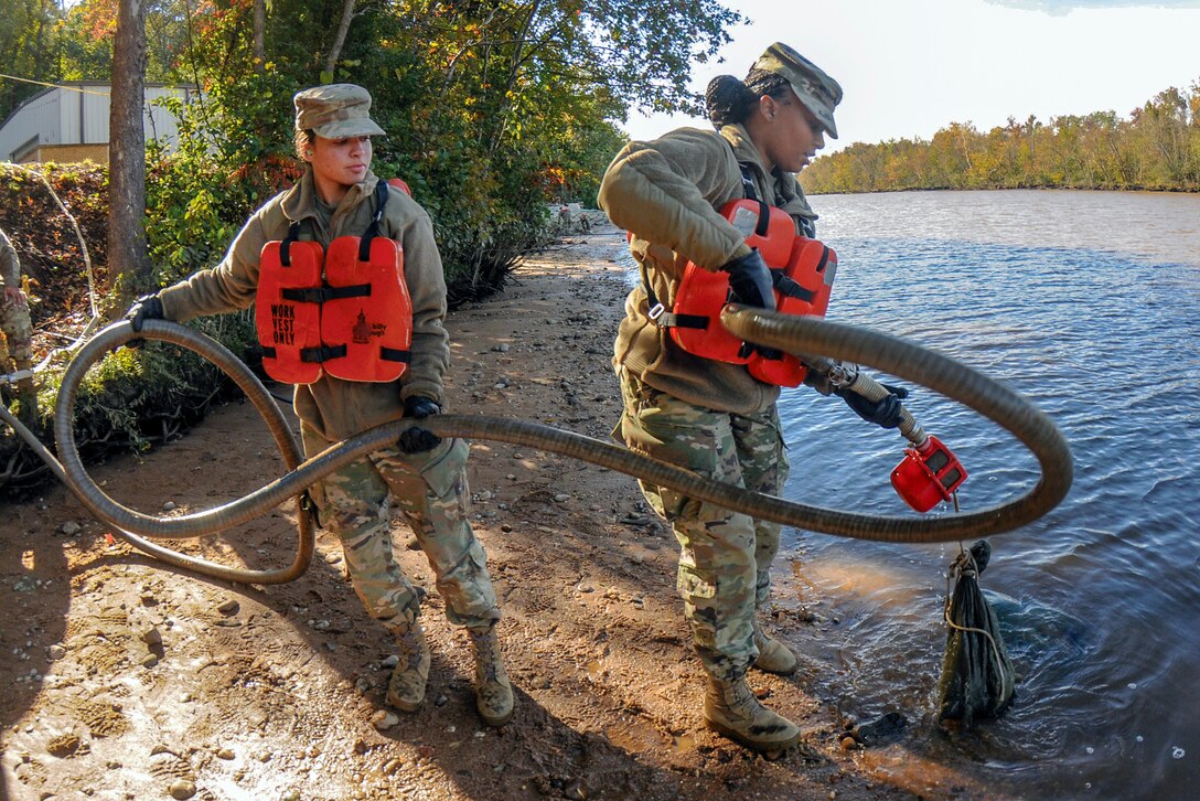 Two soldiers place a hose into a river.