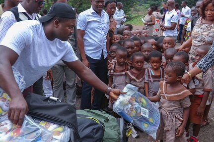 Spc. Dennis Duku hands out backpacks to school children at the Dadwen Schools Complex in western Ghana, which he attended years ago.
