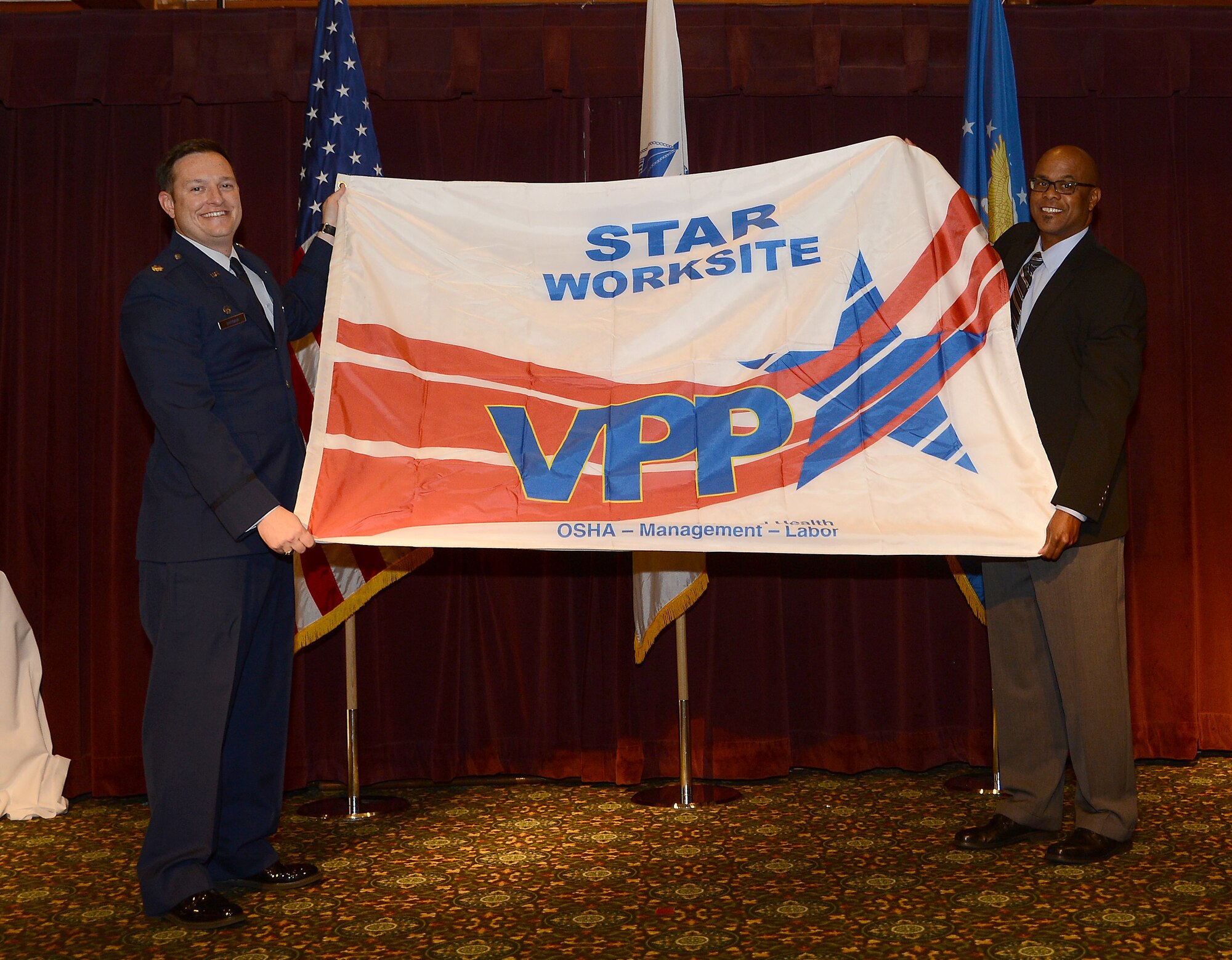 Lt. Col. Gregory Durham, 627th Logistics Readiness Squadron commander, and Darrell McKinney, 404th Army Field Support Brigade material readiness division chief, show the Voluntary Protection Program (VPP) Star Site flag to the audience Nov. 1, 2018 at Joint Base Lewis-McChord, Wash.