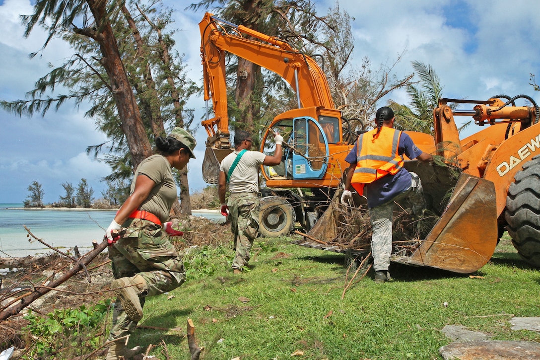 Three soldiers drag a broken branches toward a tractor.