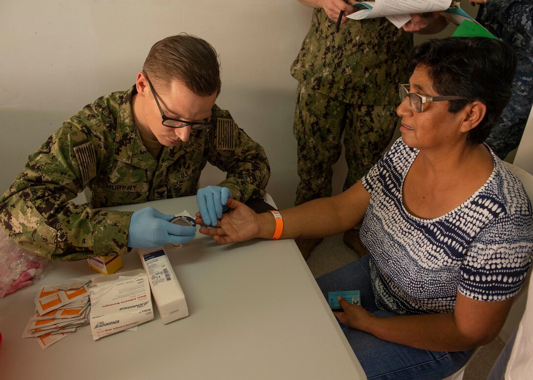 Hospital Corpsman 3rd Class Michael Murphey, from Crestline, Calif., tests a patient’s glucose levels during intake at one of two medical sites.