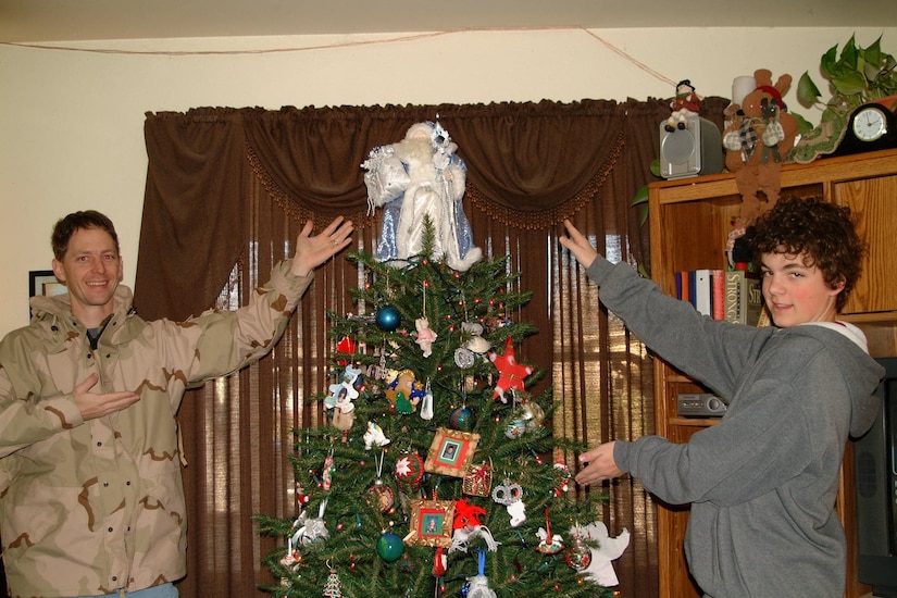 A father and son stand next to a Christmas tree.