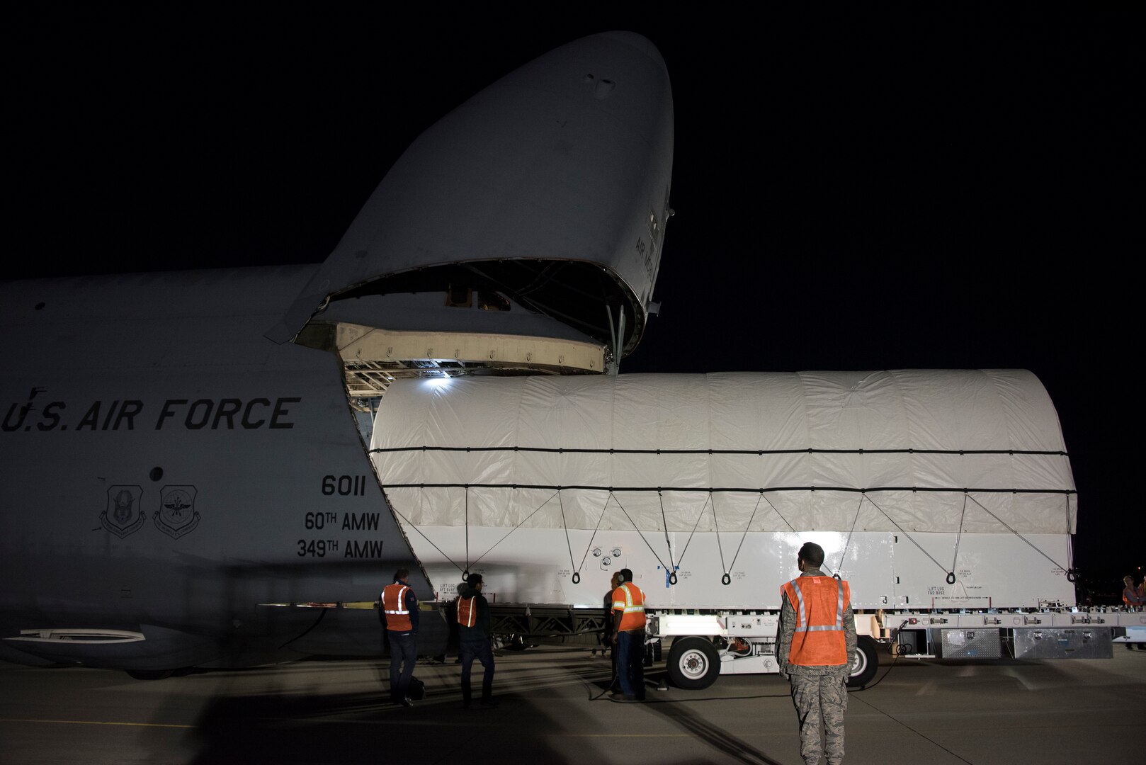 Large white wrapped item is loaded into a huge grey Air Force transport aircraft.