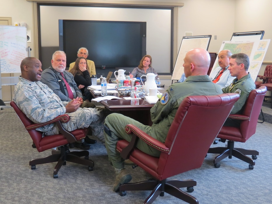 Three Airmen and five civilians around a conference table during a brief