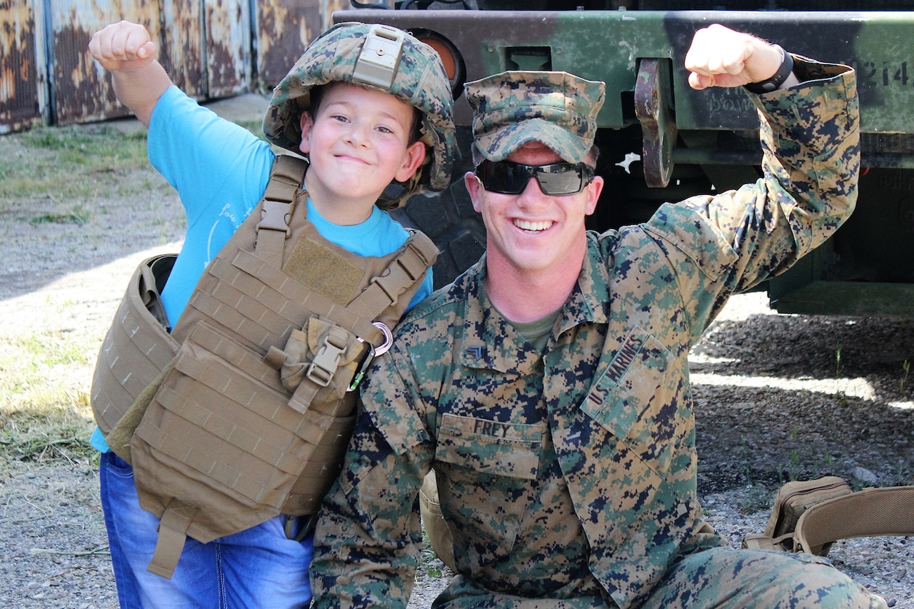 A Marine and child make muscles for the camera