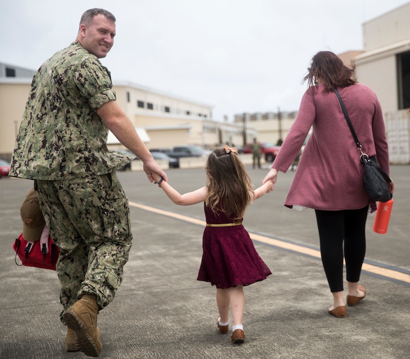 A sailor and his wife hold hands with their daughter