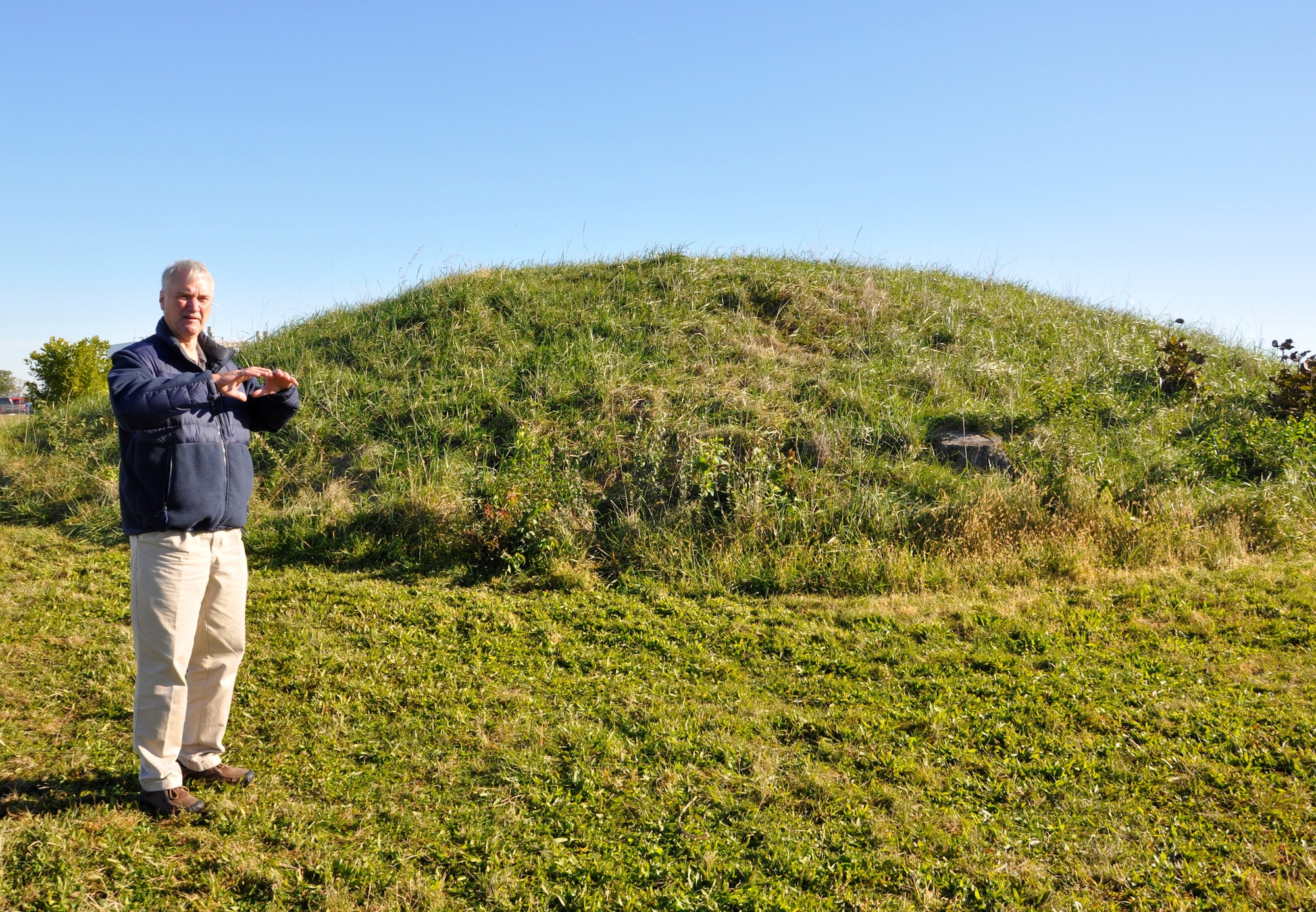 Erwin Roemer, Cultural Resources Subject Matter Specialist, stands next to the largest mound at Wright-Patterson AFB located on the north corner of Hobson Way and Ninth St., Area B. Roemer explained the Native American Tribes wanted the trees cut down so the roots would not damage the mound. This mound is the third largest mound in the Miami Valley and it is believed this mound’s location and those of the Wright Brothers Memorial were placed intentionally relative to each other. (U.S. Air Force photo/W. Eugene Barnett)