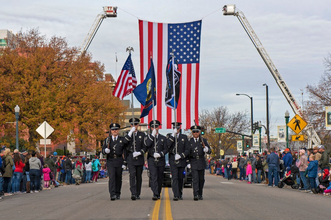 A uniformed group carrying flags march down a spectator-lined street.