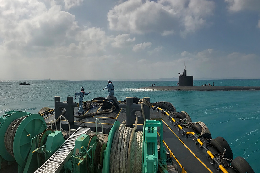 A submarine emerges ahead of a boat in the ocean.