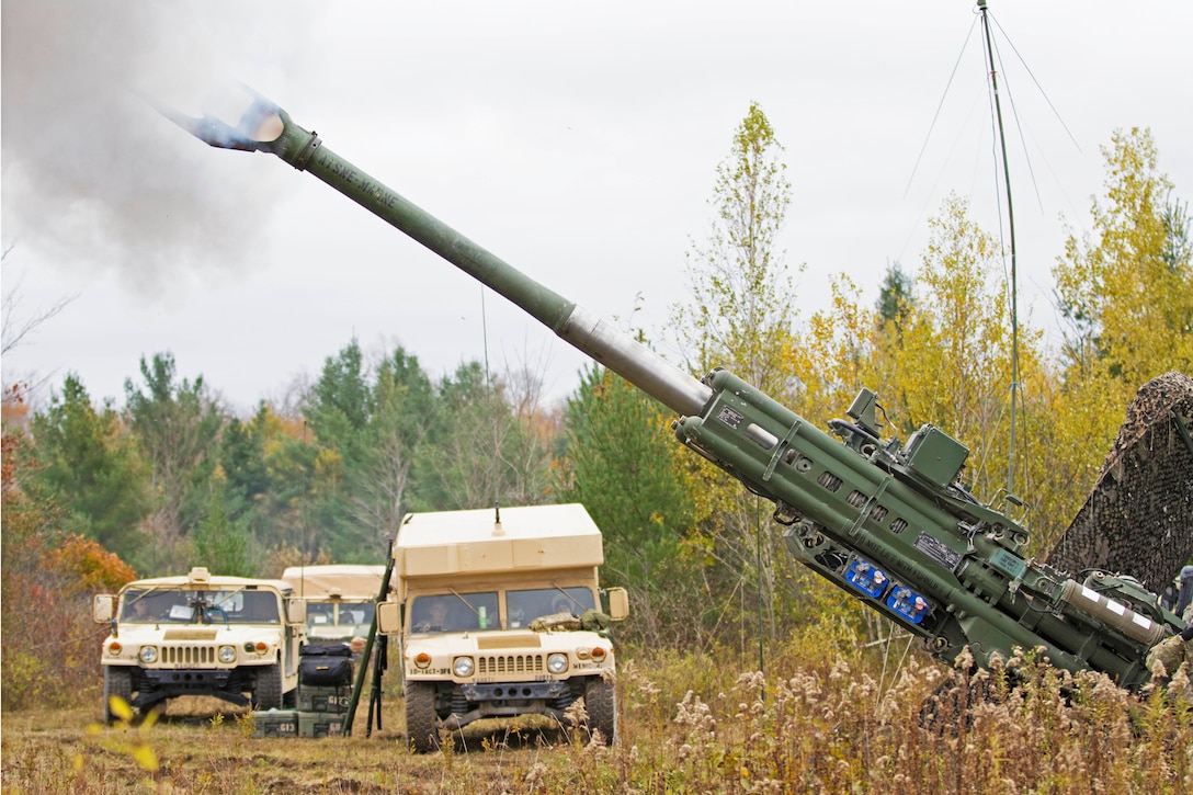 Soldiers fire artillery with two vehicles nearby.
