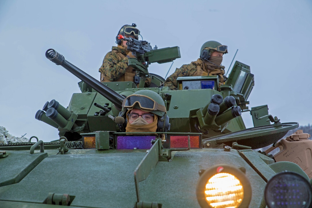 Three Marines stand watch from a tank.