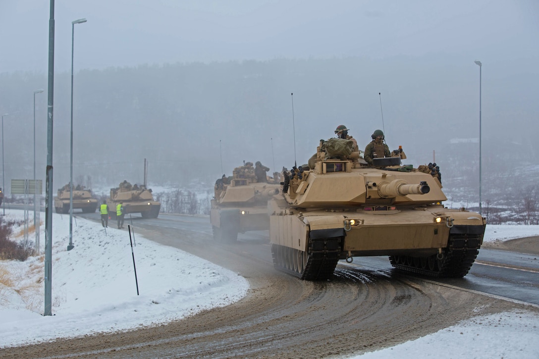 A convoy of  four tanks travel down a snowy street.