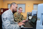 Staff Sgt. Wiggin Bernadotte, a cyber warfare operator in the Washington Air National Guard's 262nd Cyberspace Operations Squadron, works with Capt. Benjamin Kolar, a cyberspace operations officer in the 262nd, on an electrical substation simulator on Nov. 3, 2018. The 262nd is supporting Washington State Secretary of State Kim Wyman to help secure and protect voting systems for the 2018 election.