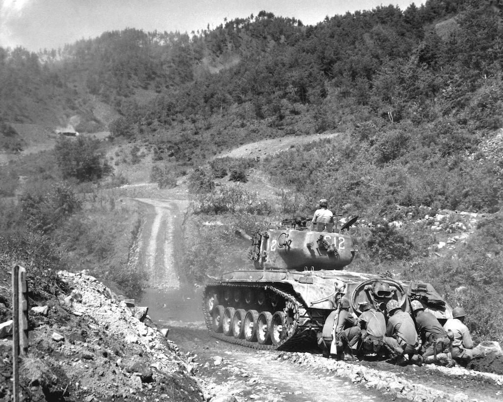 Marine infantrymen take cover behind tank while it fires on communist troops ahead, Hongchon Area, May 22, 1951 (U.S. Marine Corps/John Babyak, Jr.)