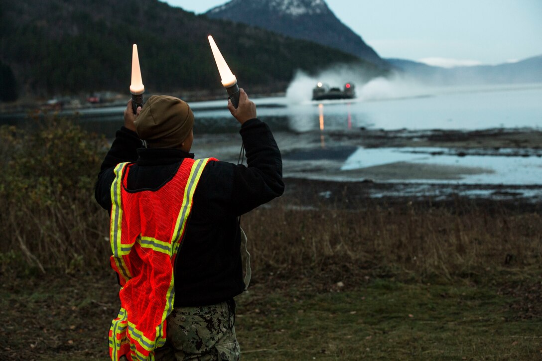 A beach master directs a landing craft air cushion during an amphibious landing in support of Trident Juncture 18 on Alvund Beach, Norway, Oct. 30, 2018. Trident Juncture provides a unique and challenging environment for Marines and Sailors to rehearse their amphibious capabilities which will result in a more ready and proficient fighting force. The LCACs originated from USS New York (LPD 21) and showcased the ability of the Iwo Jima Amphibious Ready Group and the 24th Marine Expeditionary Unit to rapidly project combat power ashore. (U.S. Marine Corps photo by Lance Cpl. Margaret Gale)