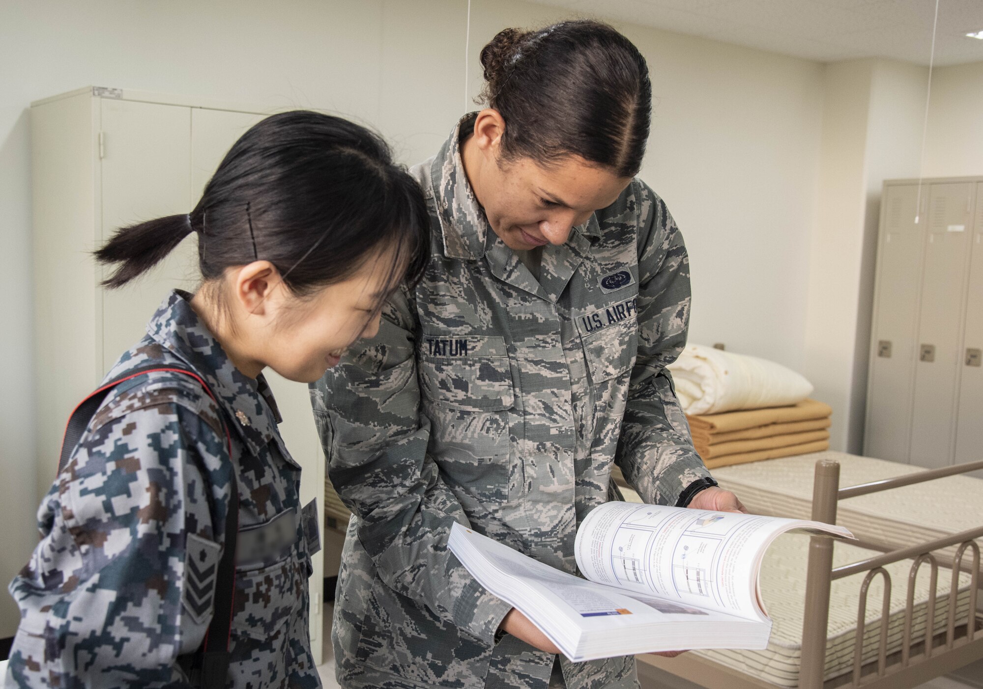 Japan Air Self-Defense Force Senior Airman Shimizu, left, a 37th Surveillance Squadron radar maintenance technician, looks at a Japanese phrase book with U.S. Air Force Airman 1st Class Hannah Tatum’s, a 35th Communications Squadron radio frequency transmission systems technician, during a bilateral exchange program at Yamada Sub Base, Yamada Town, Japan, Oct. 17, 2018. U.S. Air Force members from various career fields stayed with their JASDF counterparts to better integrate with each other. Participants obtained a deeper understanding of cultural differences among themselves and learned to perform tasks together, ensuring fluid mission execution in the future. (U.S. Air Force photo by Senior Airman Sadie Colbert)