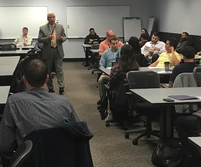 Defense Logistics Agency Land and Maritime Acquisition Executive Mark Brown speaks to a room of new associates.