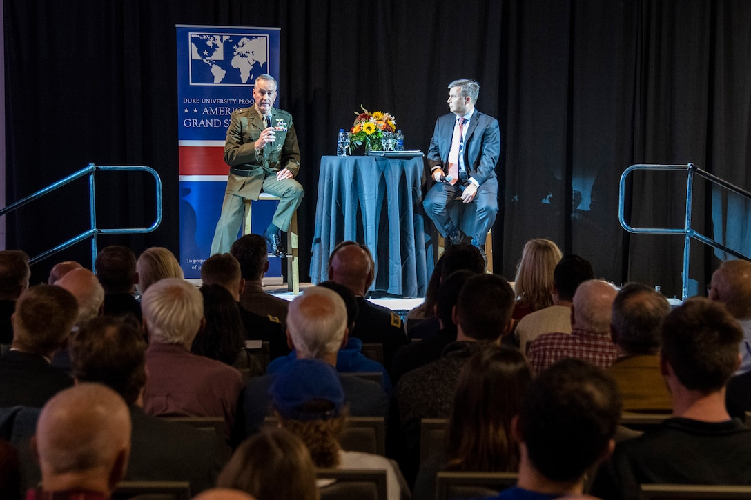 Marine Corps Gen. Joe Dunford sits with another man on a stage and speaks to an audience.